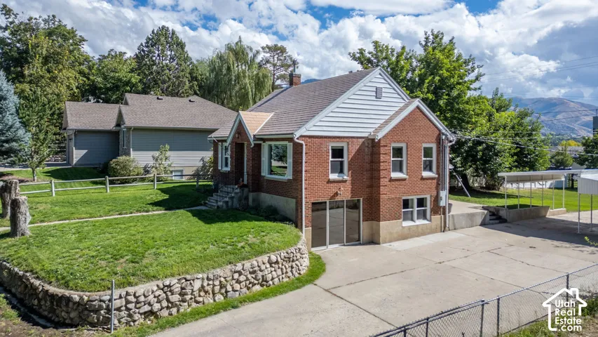 Red brick exterior with white gable siding, established landscaping, stone retaining wall, and a paved drive