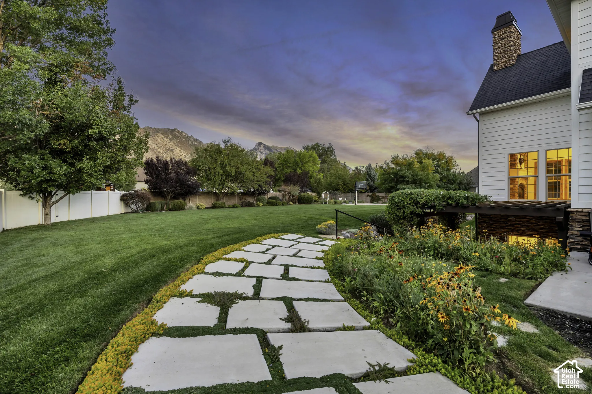 Expansive green lawn, stone paver pathway, mature trees, established garden beds, and mountain backdrop