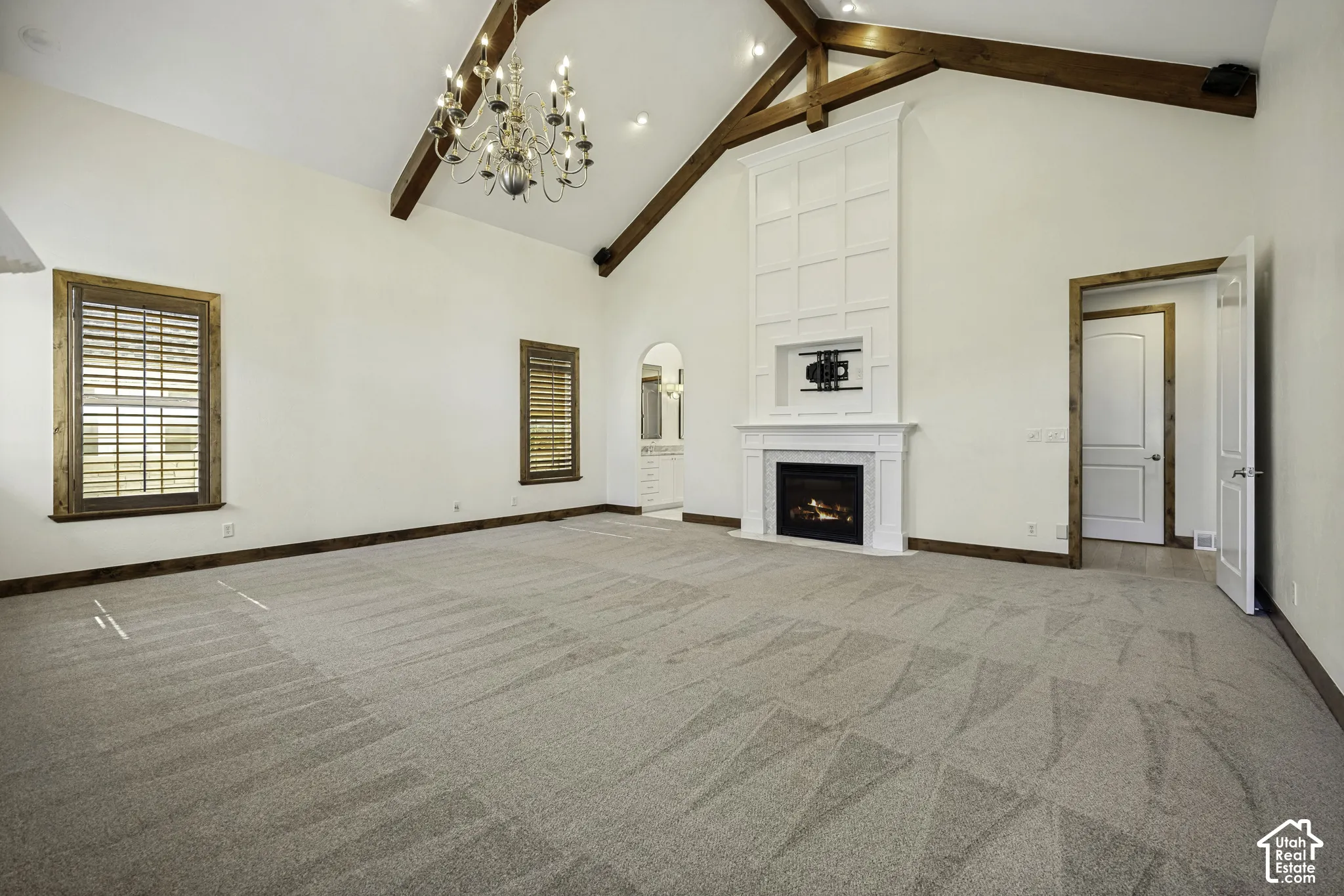 Primary Suite. Vaulted ceiling with exposed wood beams, white paneled fireplace, chandelier, and wood-framed windows