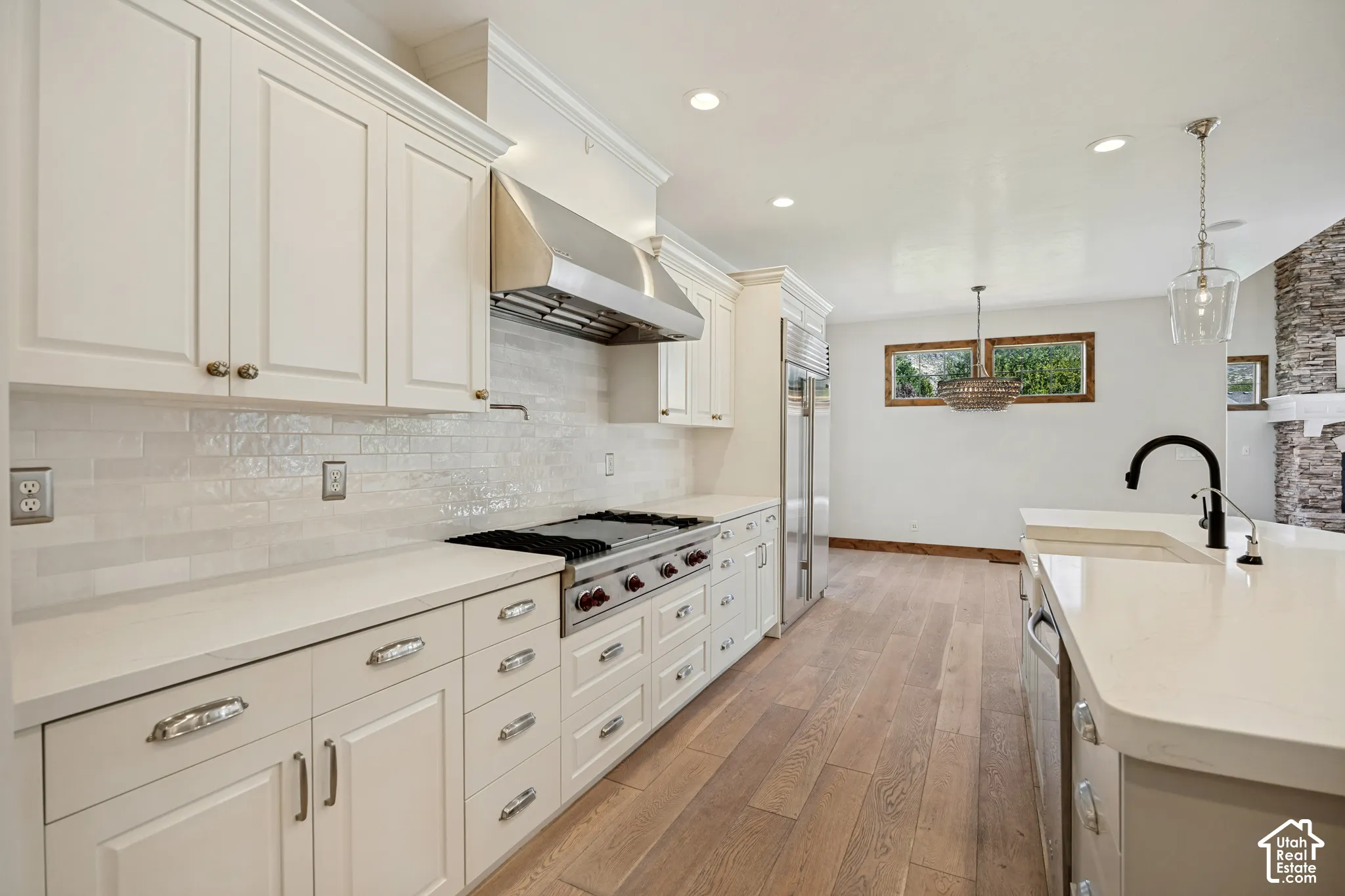 White cabinetry, stainless steel appliances, light wood-finish flooring, white countertops, and a white subway tile backsplash