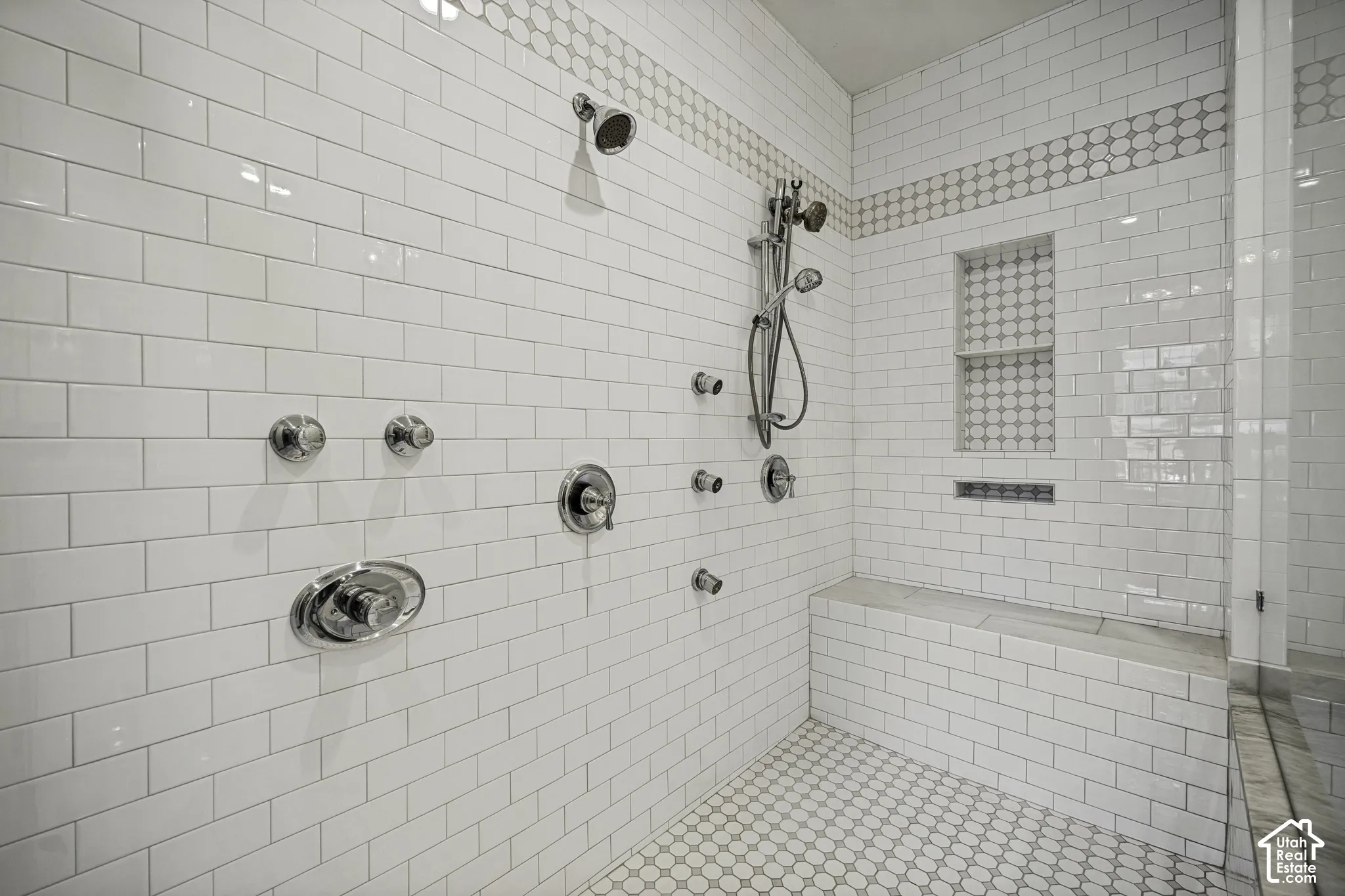 Shower featuring white subway tile, a built-in bench, recessed shelf, and multiple polished chrome fixtures