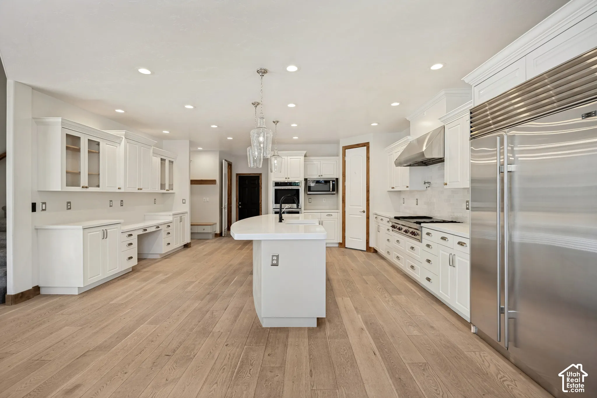 Gourmet kitchen with wood-finish flooring, white cabinetry, stainless steel appliances, a center island with pendant lighting, and recessed lighting