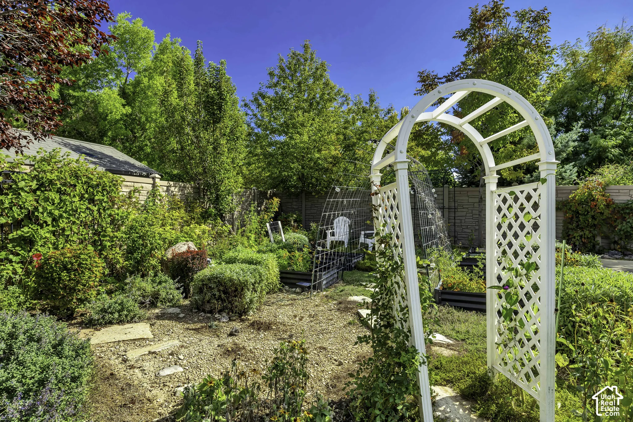 Landscaped backyard featuring an arched trellis entrance, raised garden beds, and mature perimeter trees