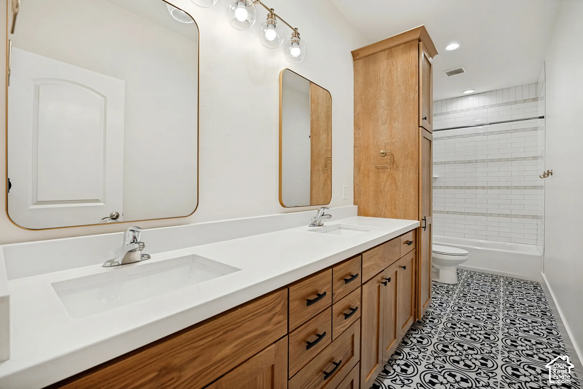 Dual vanity with integrated rectangular sinks, wood-finish cabinetry with dark hardware, quartz countertop, patterned floor tile, and subway tile tub surround