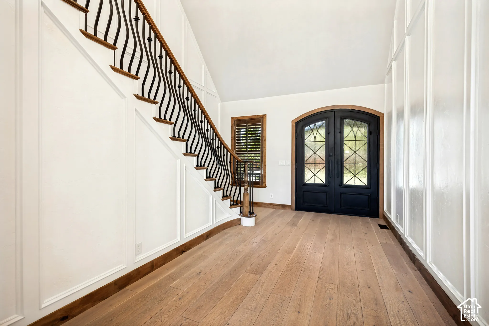 Grand entryway featuring a curved staircase with wrought iron balusters, light wood-finish flooring, and paneled walls