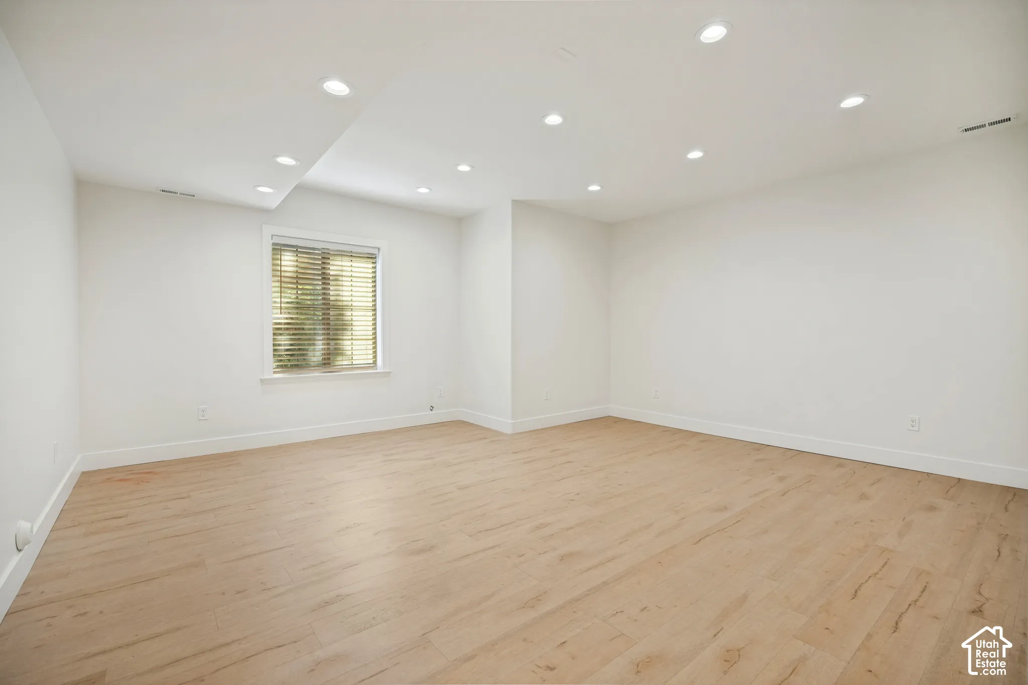 Recessed lighting illuminates the spacious room with light wood-finish flooring
