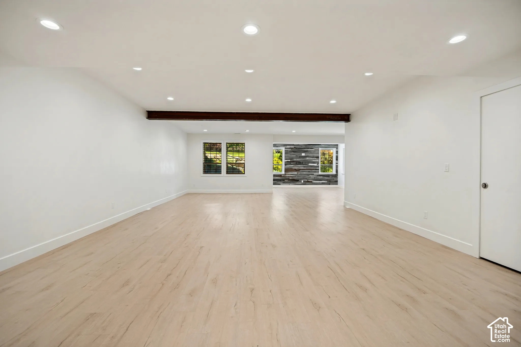 Recessed ceiling lighting, wood-finish flooring, exposed wood beam, multiple windows, and a white interior door