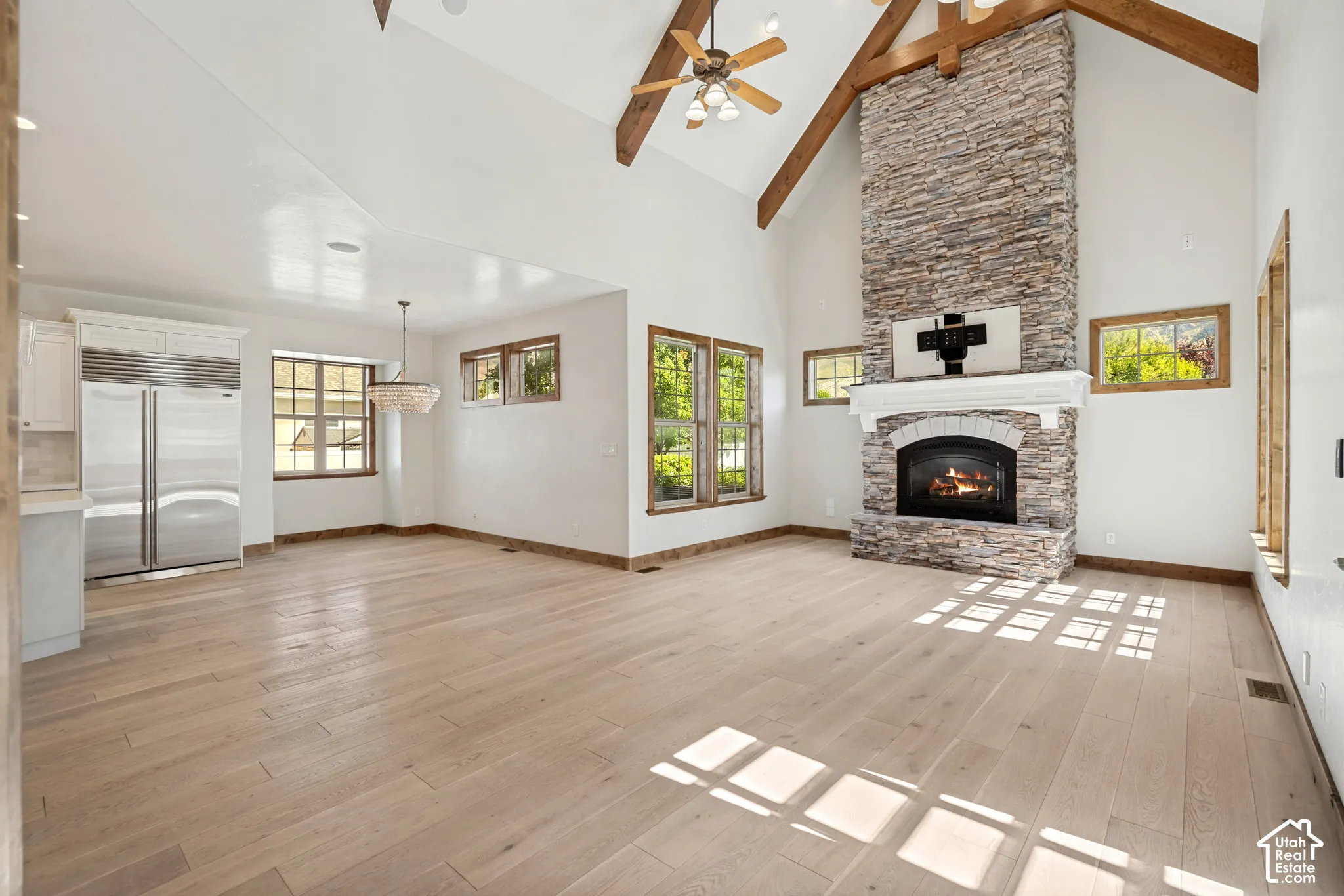 Vaulted ceilings with exposed wood beams, a stone-clad fireplace, light wood-finish flooring, and multiple windows with wood-framed trim