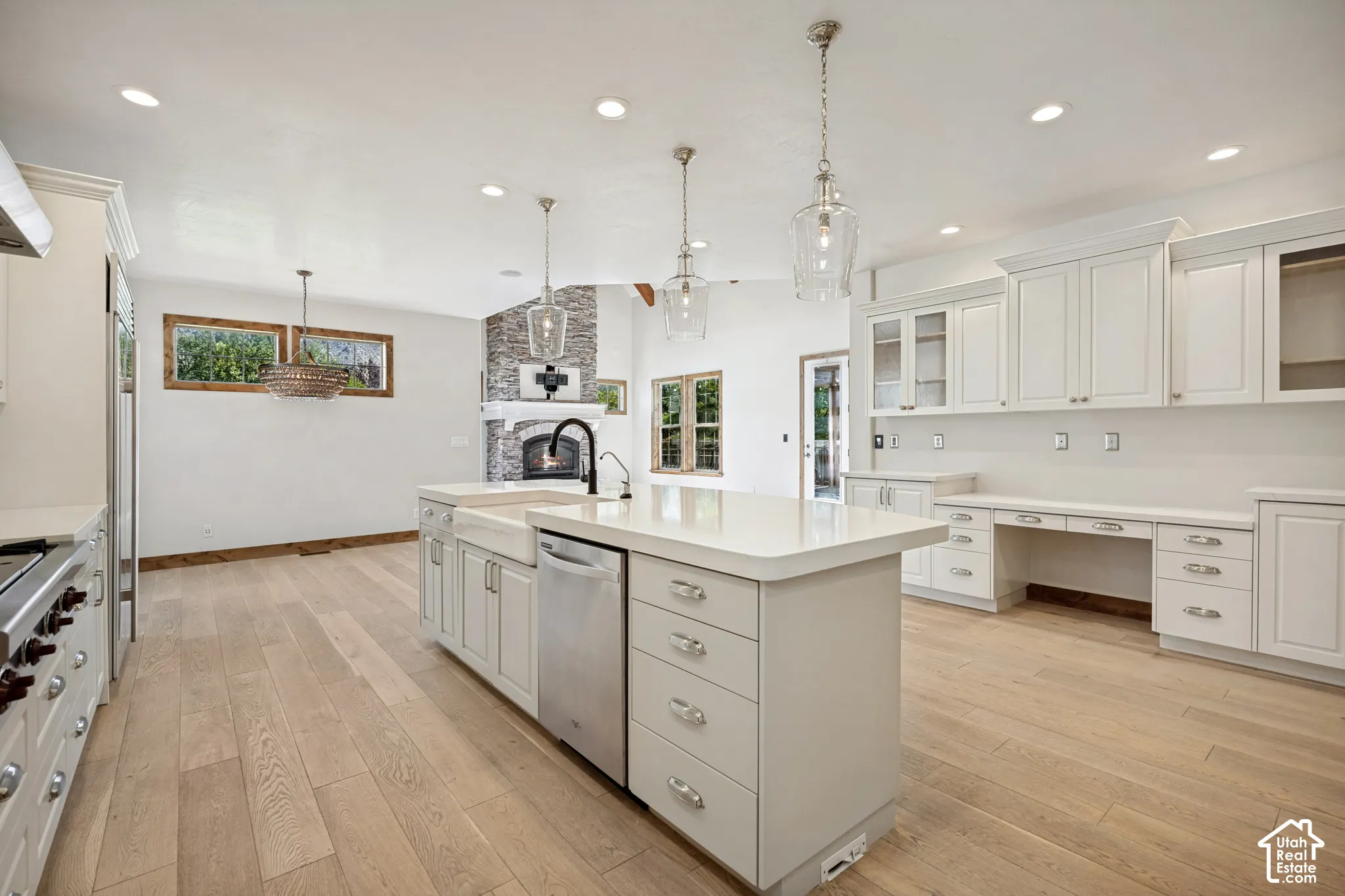 Expansive kitchen featuring a large island with an integrated farmhouse sink, light wood-finish flooring, recessed lighting, and built-in white cabinetry with a dedicated desk area