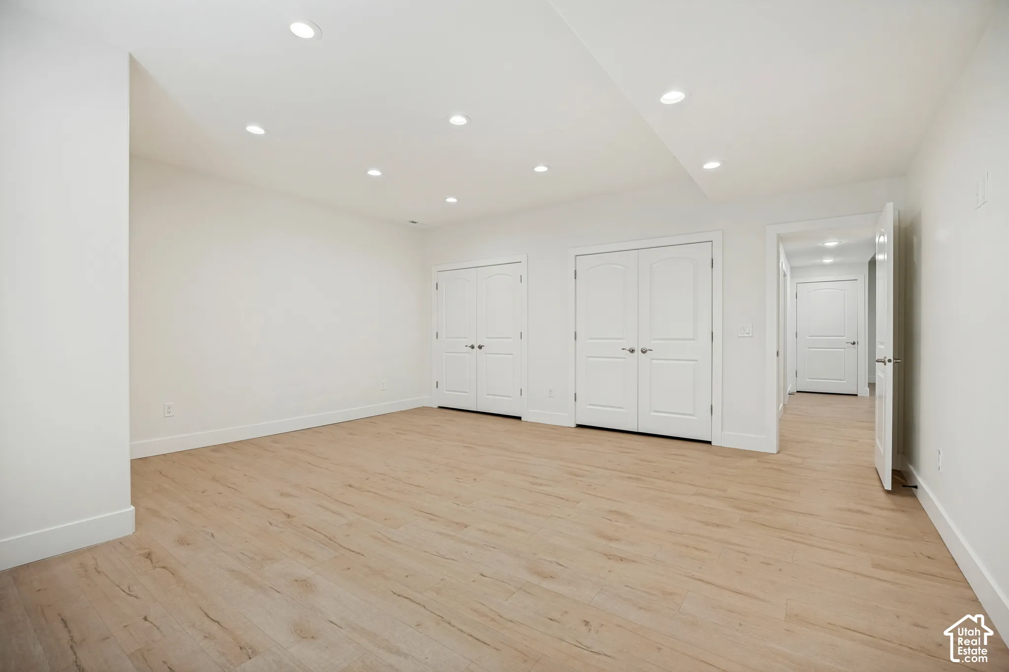 Recessed ceiling lighting, light wood-finish flooring, white walls, white bi-fold doors, and a white interior door
