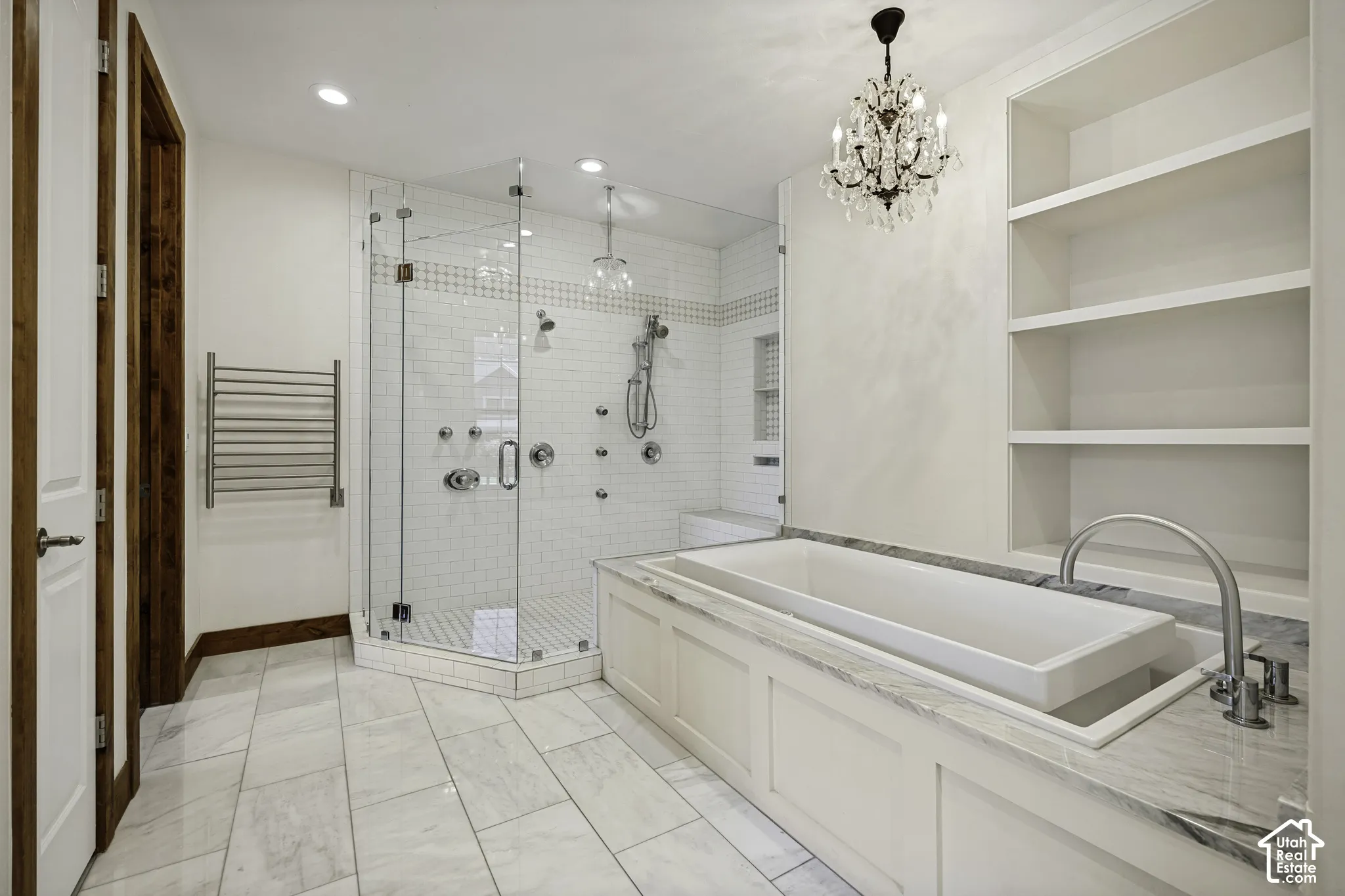 Built-in soaking tub with a stone countertop, expansive glass-enclosed shower with multiple showerheads, white subway tile, and a crystal chandelier