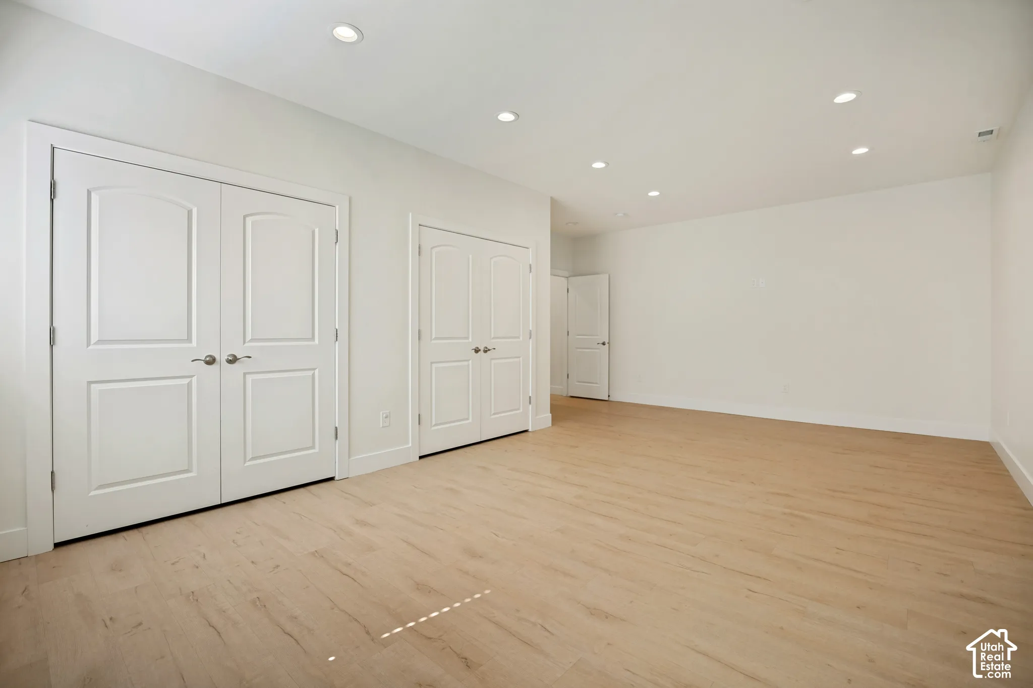 Recessed lighting, light wood-finish flooring, white walls, and multiple panel doors with hardware