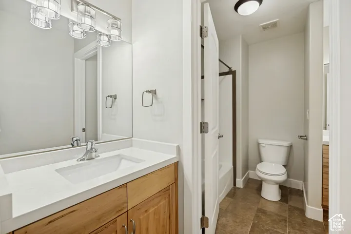 Vanity with a white countertop and integrated sink, wood-finish cabinetry, a large wall mirror, and a modern vanity light fixture