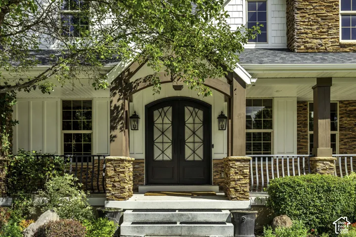 Arch-top double entry doors with decorative glass, stone veneer accents, board and batten siding, multiple windows with grilles, and a covered porch