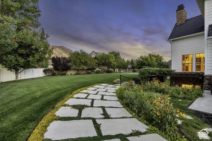 Expansive green lawn, stone paver pathway, mature trees, established garden beds, and mountain backdrop