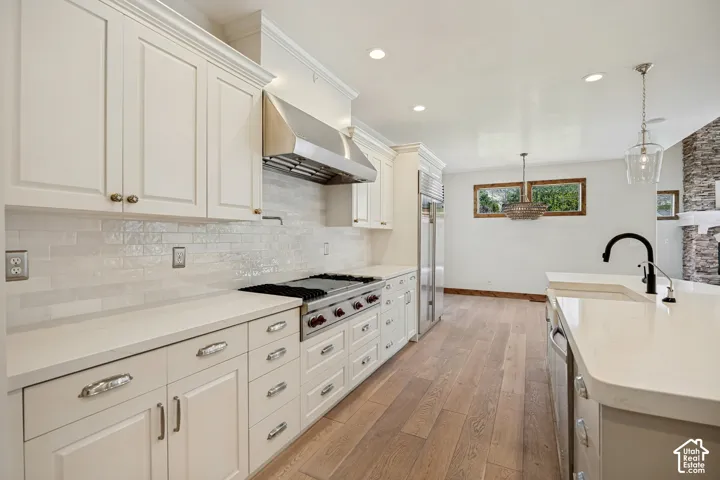 White cabinetry, stainless steel appliances, light wood-finish flooring, white countertops, and a white subway tile backsplash