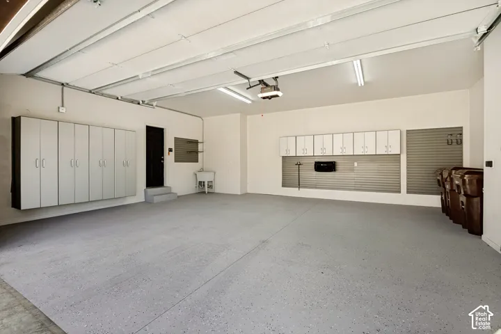 Spacious garage featuring a finished epoxy floor, built-in cabinetry, slatted wall storage systems, and a utility sink