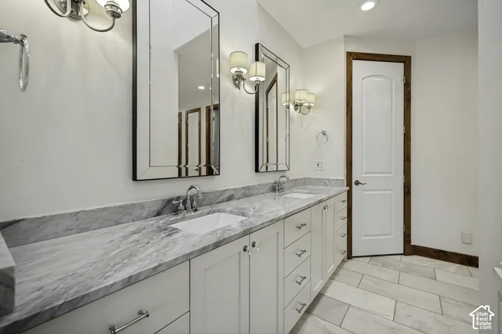 Dual vanity with integrated sinks, polished chrome fixtures, white cabinetry, and a stone countertop