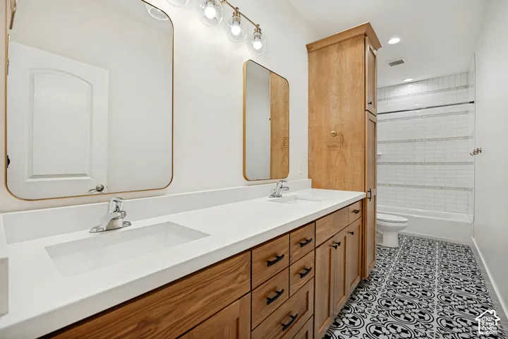 Dual vanity with integrated rectangular sinks, wood-finish cabinetry with dark hardware, quartz countertop, patterned floor tile, and subway tile tub surround