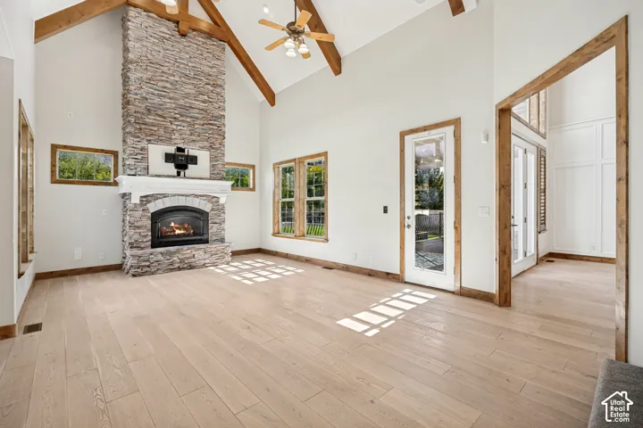Vaulted ceiling with exposed wood beams, stone fireplace, wood-finish flooring, and white walls