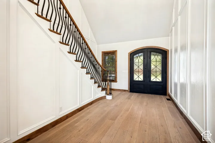 Grand entryway featuring a curved staircase with wrought iron balusters, light wood-finish flooring, and paneled walls