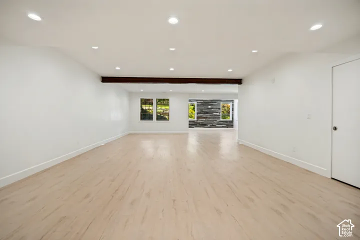 Recessed ceiling lighting, wood-finish flooring, exposed wood beam, multiple windows, and a white interior door