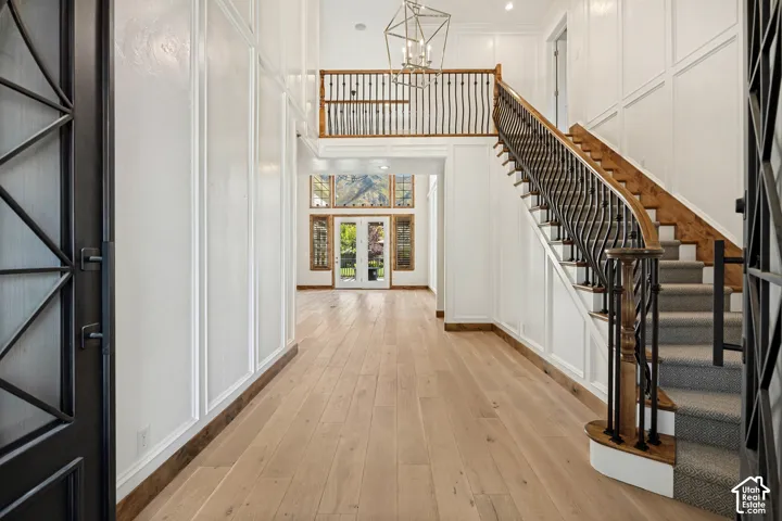 Two-story entryway featuring a grand staircase with wrought iron balusters, wood-finish flooring, white paneled walls, and a decorative chandelier