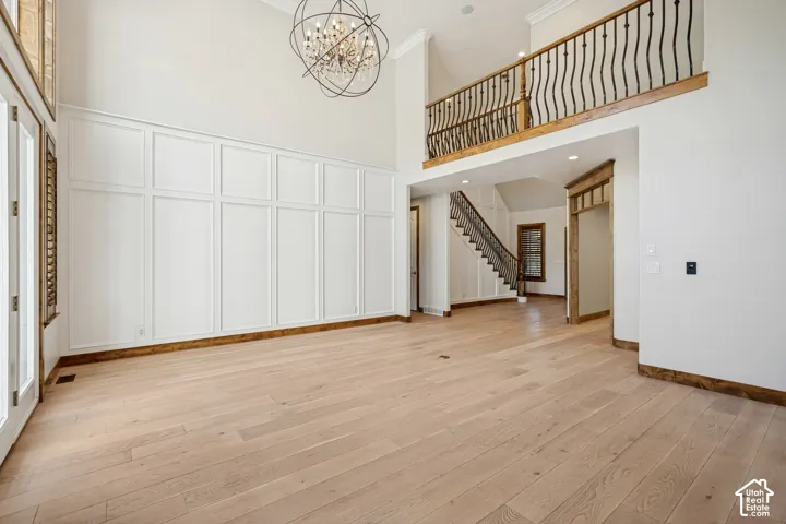 High ceilings with an exposed beam, light wood-finish flooring, white wainscoting, and a wrought iron chandelier