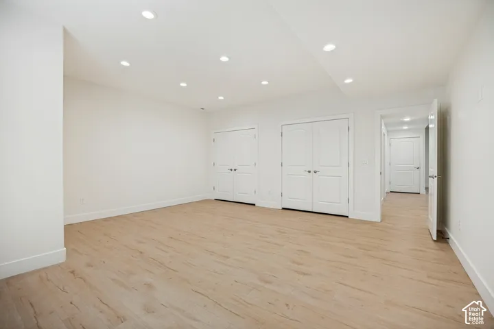 Recessed ceiling lighting, light wood-finish flooring, white walls, white bi-fold doors, and a white interior door
