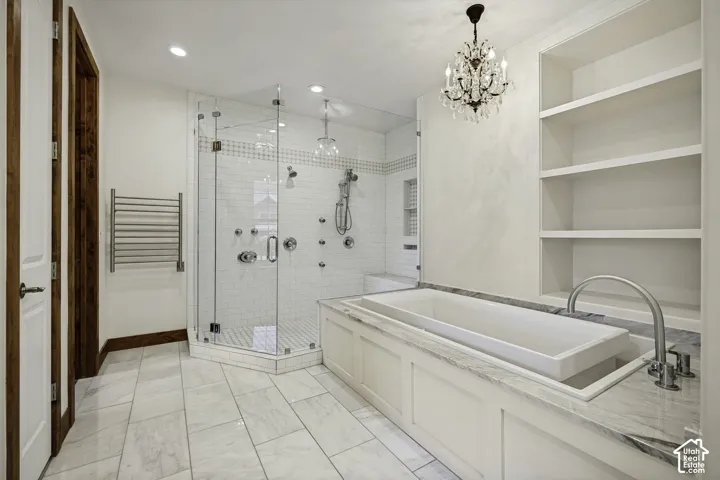 Built-in soaking tub with a stone countertop, expansive glass-enclosed shower with multiple showerheads, white subway tile, and a crystal chandelier
