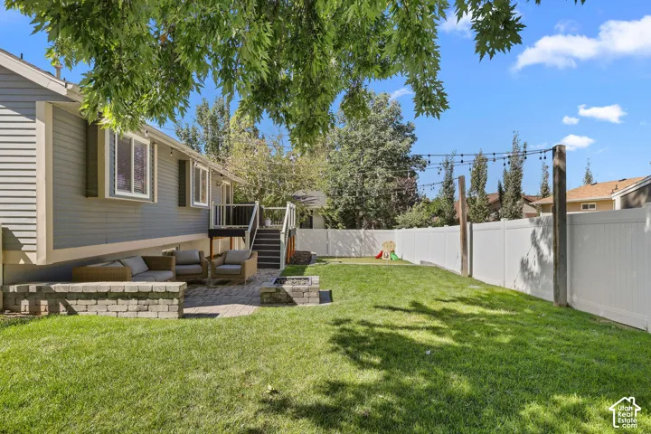 Expansive backyard featuring a manicured lawn, white privacy fencing, and a paver patio with a stone-finish retaining wall