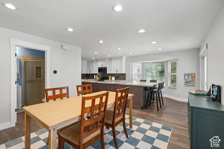 Recessed lighting illuminates wood-finish flooring, a kitchen island with seating, a bay window, and white cabinetry