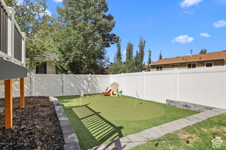 Expansive backyard featuring a putting green, white privacy fencing, and a raised planter bed