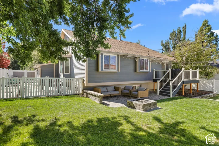 Expansive green lawn with a white picket fence, a stone-paved patio, and a built-in stone fire pit