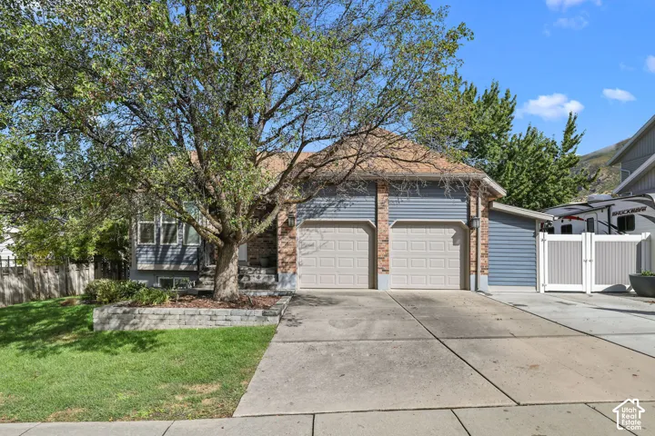 Exterior featuring siding and brick accents, an attached two-car garage, a mature tree, and a paved driveway