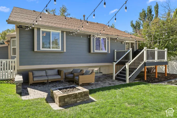 Expansive paver patio with a built-in stone fire pit, leading to a multi-level deck with white and black railings