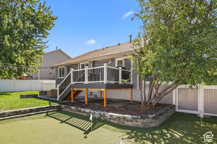 Rear exterior featuring a multi-level deck with white and black railings, an artificial turf putting green, a stone retaining wall, and a privacy fence