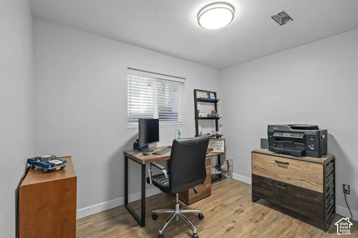 Light gray walls, wood-finish flooring, a window with horizontal blinds, and a flush-mount ceiling light