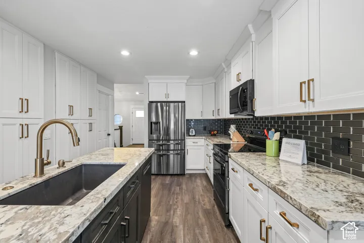 Kitchen featuring white cabinetry, a dark tile backsplash, stainless steel appliances, a center island with a dark sink, and wood-finish flooring
