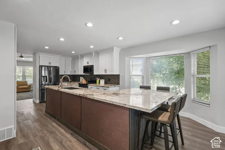 Kitchen featuring an expansive island with a light-toned countertop, white upper cabinetry, dark wood-finish lower cabinetry, and wood-finish flooring