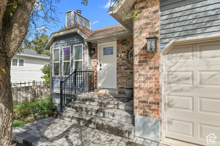Brick and siding exterior with a paneled garage door, paver pathway, and detailed front steps with a metal railing