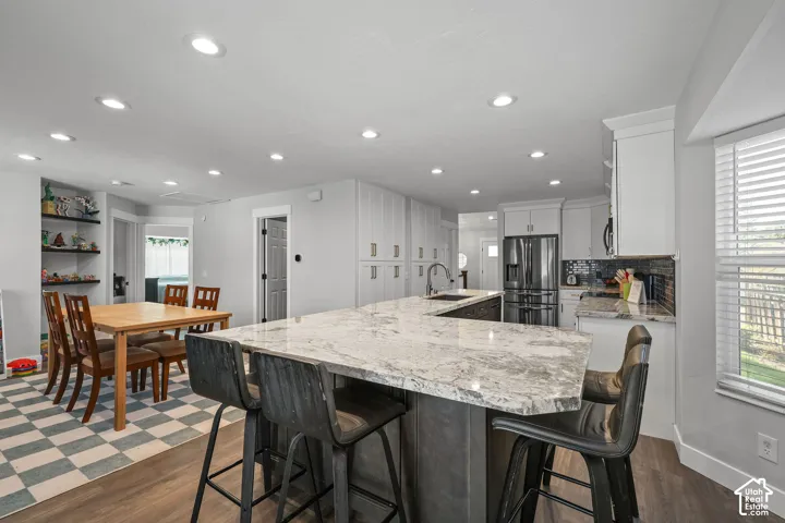 Expansive kitchen island with a light-toned countertop, recessed lighting, wood-finish flooring, white cabinetry, and stainless steel appliances