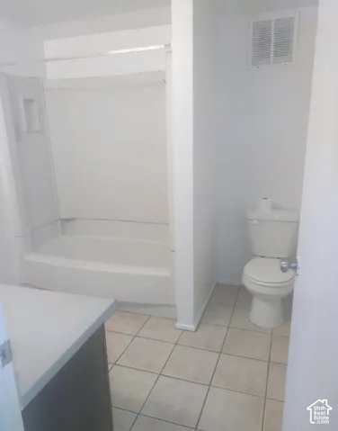 Bathroom featuring a white shower-tub combination, a white toilet, a vanity with a light-colored countertop, and square tile flooring