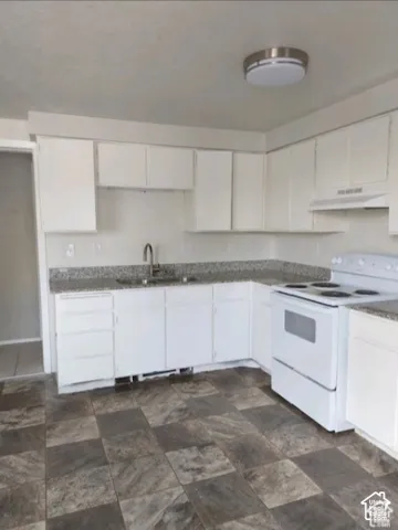 White cabinetry, granite-style countertops, stainless steel sink with a high-arc faucet, white range, and multi-tone tile flooring