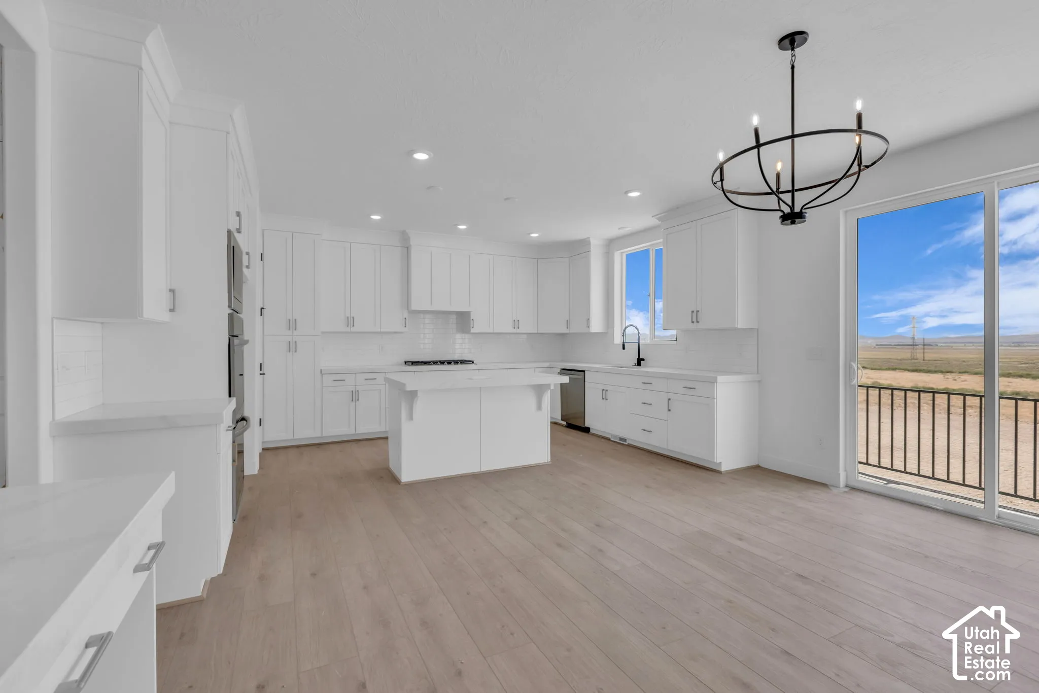 Spacious kitchen featuring full-height cabinetry, a central island, and stainless steel gourmet appliances to include a gas cooktop and double ovens. Spacious dining with large custom sliding patio door.