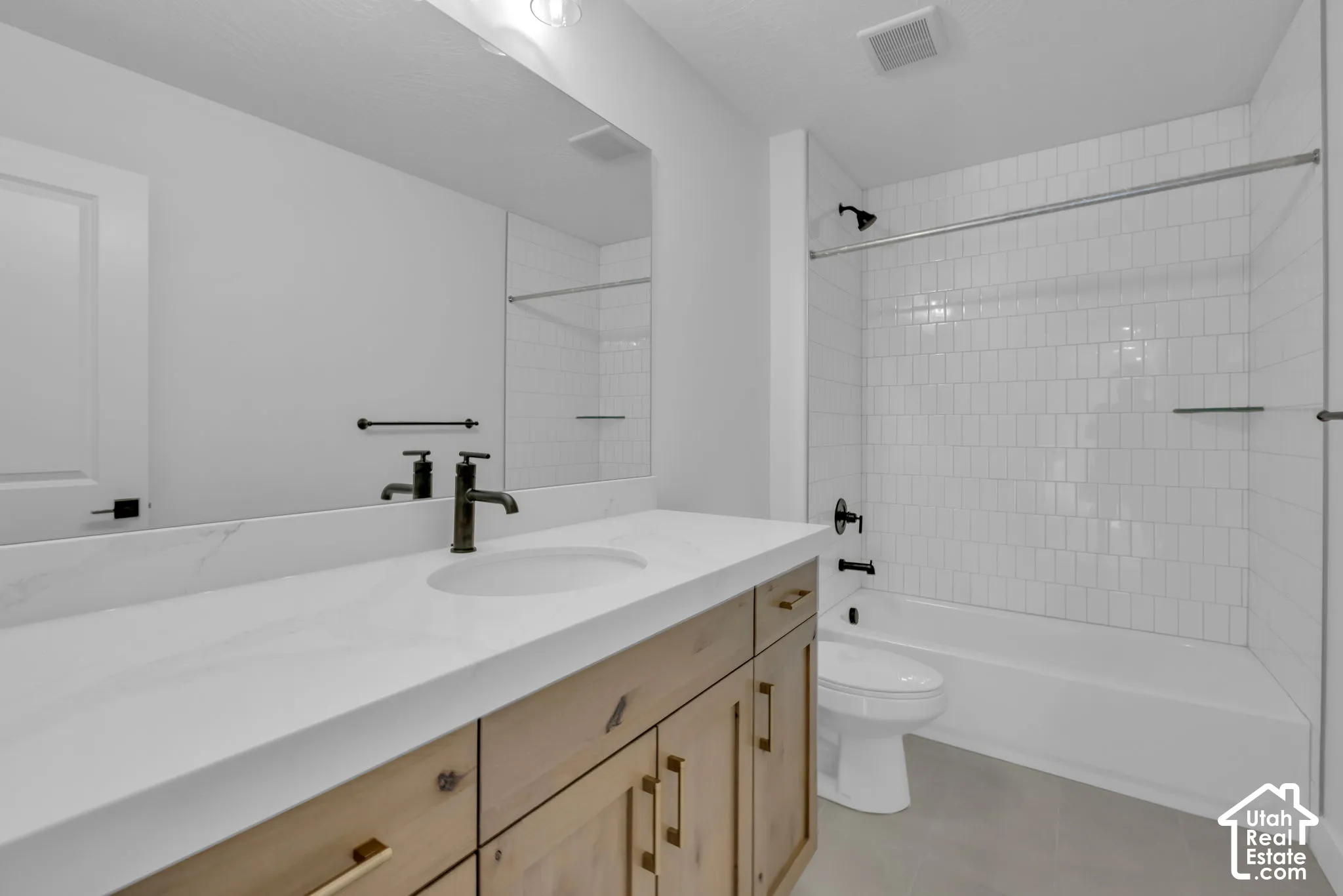 Two of two secondary bathrooms with white subway tile shower surround and natural stained cabinets and oversized quartz countertops.