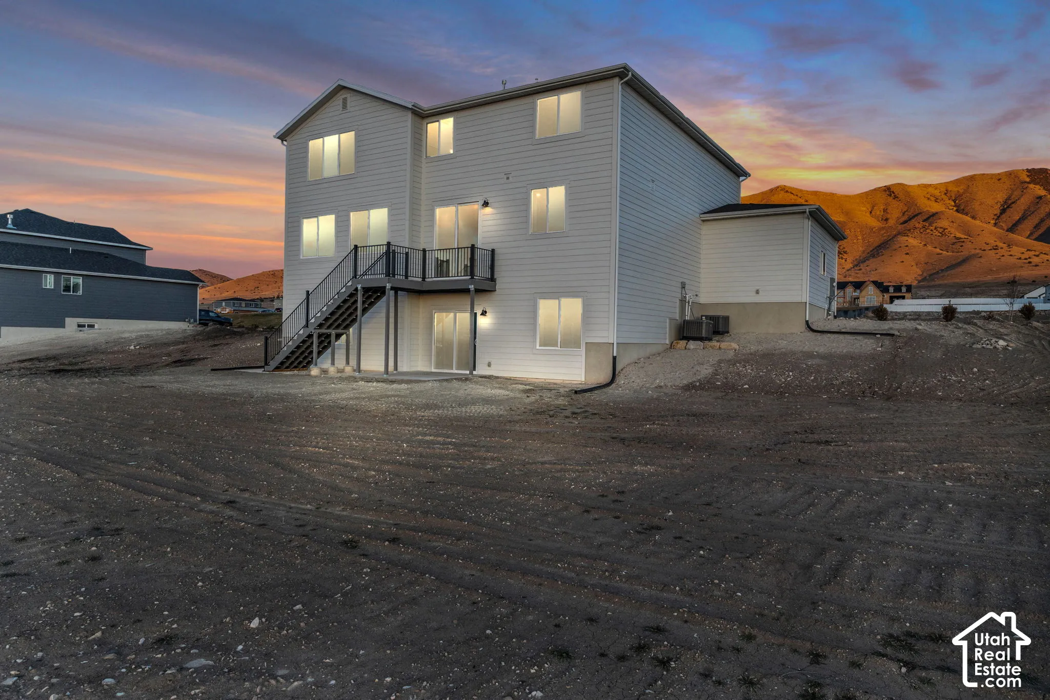 Back of home from the southwest corner showing second-story deck, black railing, and exterior staircase.  Home includes a walkout basement to a flat backyard on a .75 acre lot.