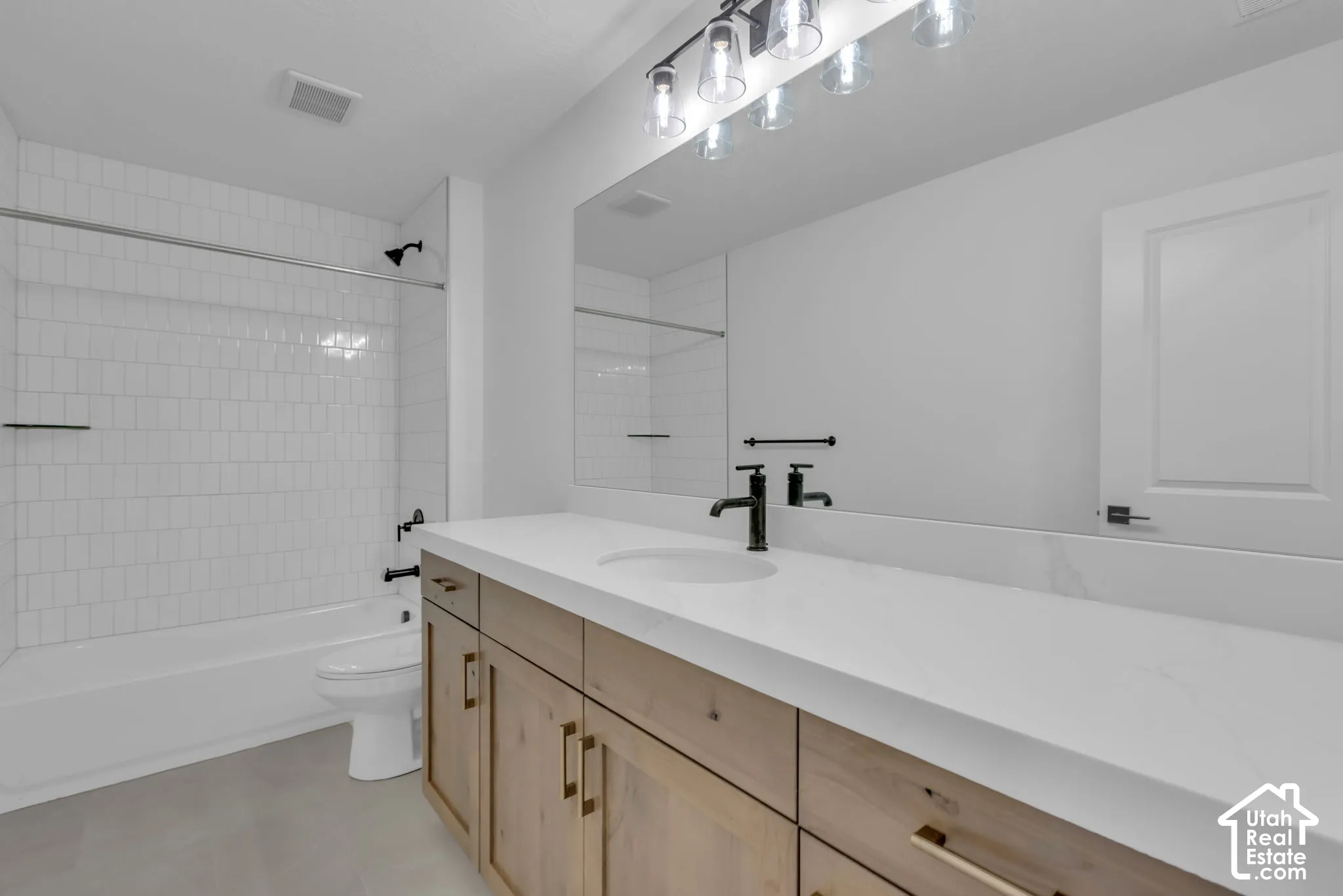 One of two secondary bathrooms with white subway tile shower surround and natural stained cabinets and oversized quartz countertops.