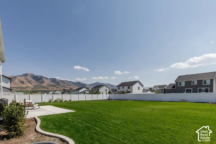 Expansive green lawn, concrete patio, white privacy fencing, and mountain backdrop
