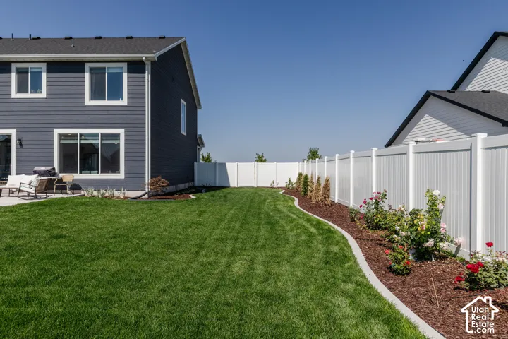 Expansive lawn featuring a concrete patio, white vinyl fencing, and a mulched garden bed with blooming shrubs